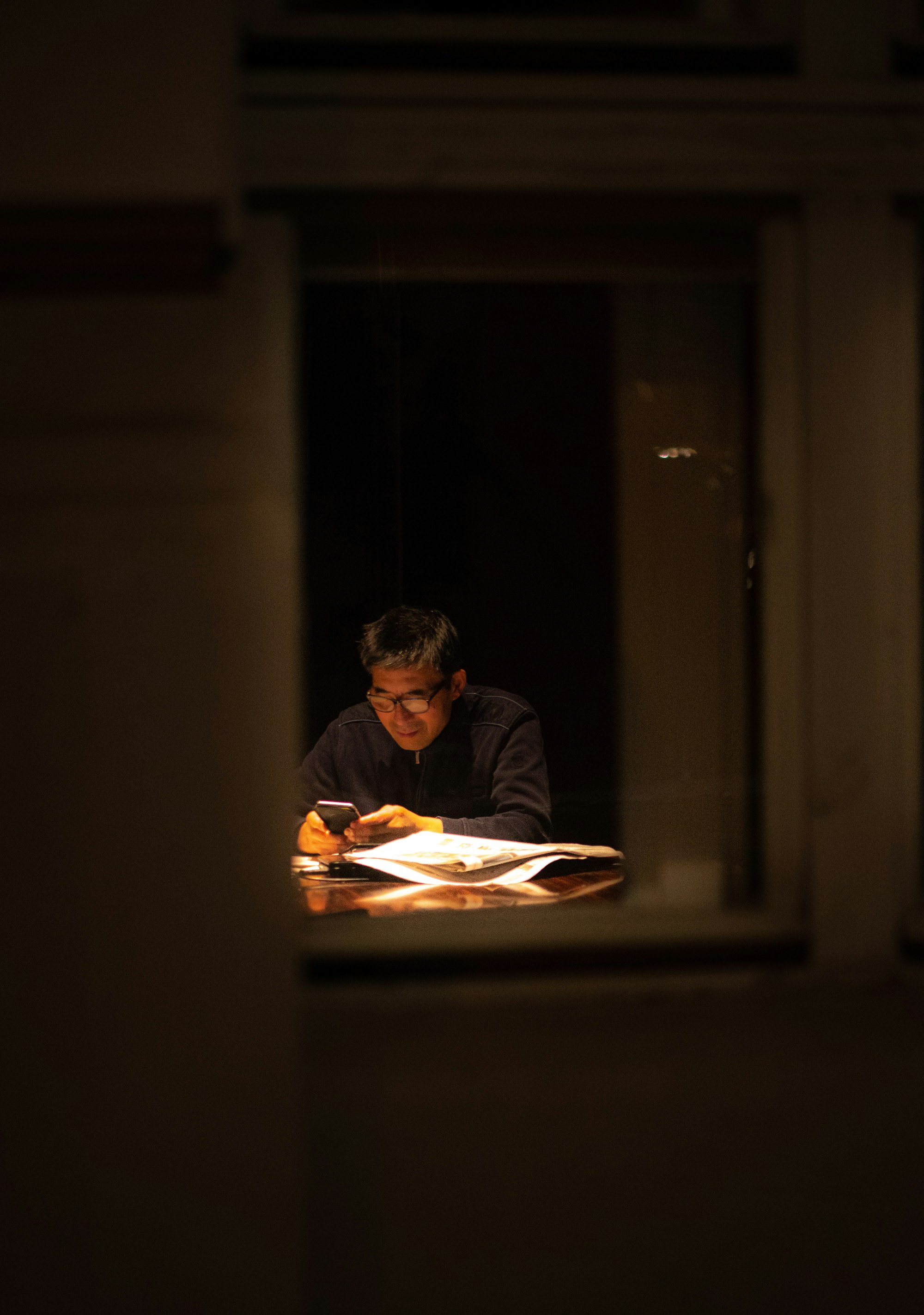 A desk lit for late reading, seen through a night window