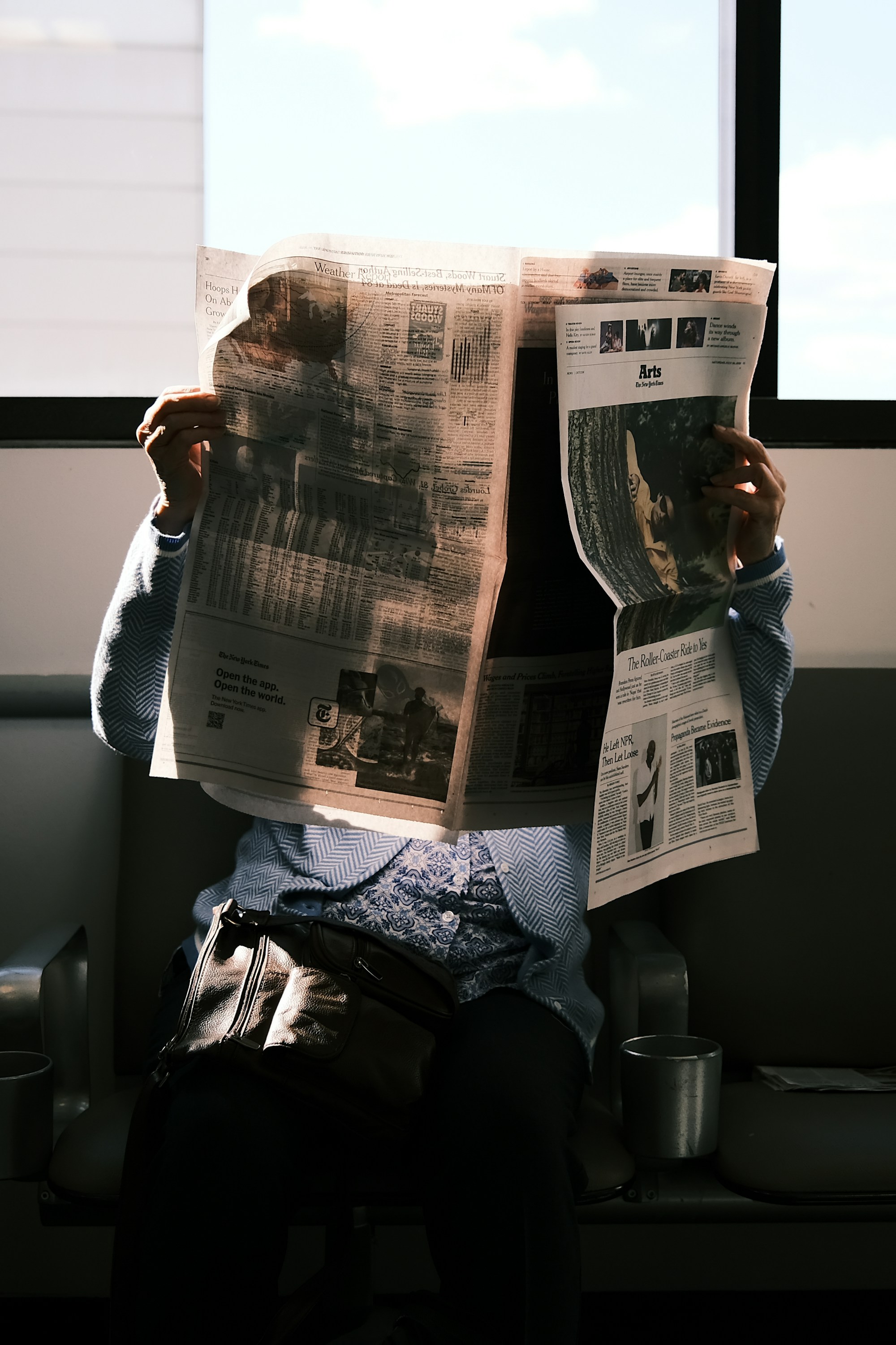 A reader holding a broadsheet open against a bright window